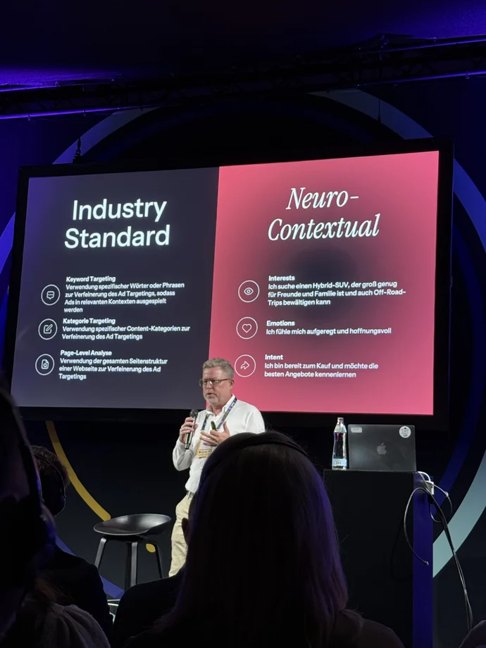 Präsentation über Keyword Targeting vs. Neuro-Contextual im Marketing, Mann spricht auf der Bühne mit Folien im Hintergrund.