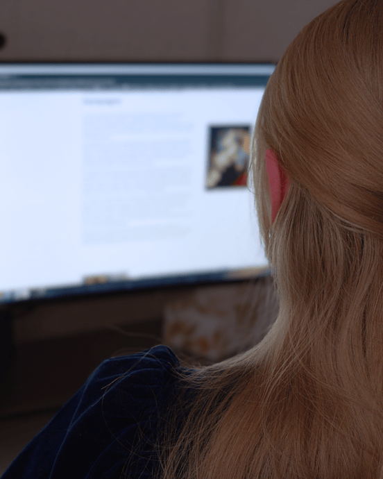 Person arbeitet an einem Computer mit zwei Bildschirmen, liest Textinhalt.