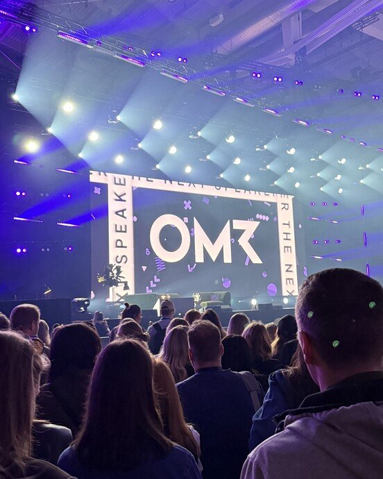 Menschenmenge bei OMR-Veranstaltung in einem großen, lichtdurchfluteten Saal mit Bühne und LED-Anzeige.