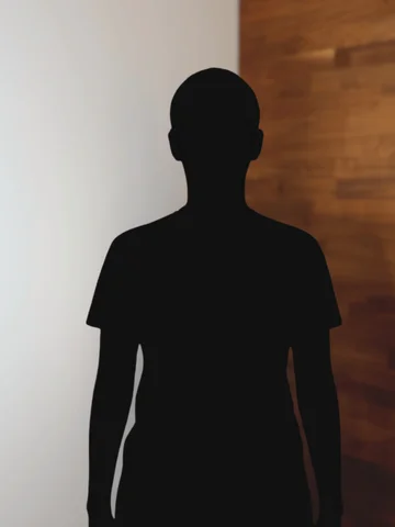 Silhouette einer Person vor zweigeteilter Wand, links hell, rechts dunkelholzfarben.