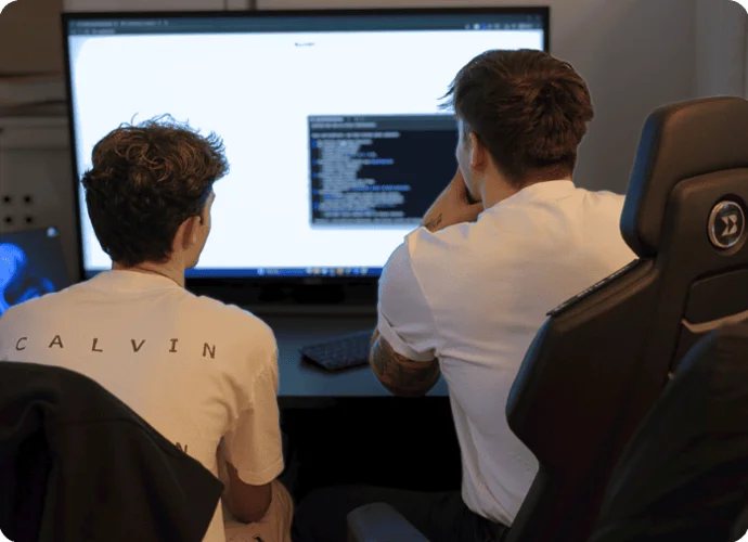 Zwei Personen betrachten einen Computerbildschirm mit Code in einem Büro.