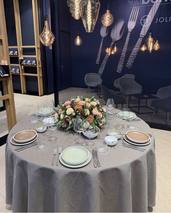 Eleganter, gedeckter Tisch mit Blumenarrangement, umgeben von modernen Lampen und wandseitigen Deko-Elementen.