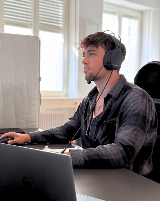 Mann mit Kopfhörern arbeitet konzentriert an Computerbildschirmen in einem Büro.