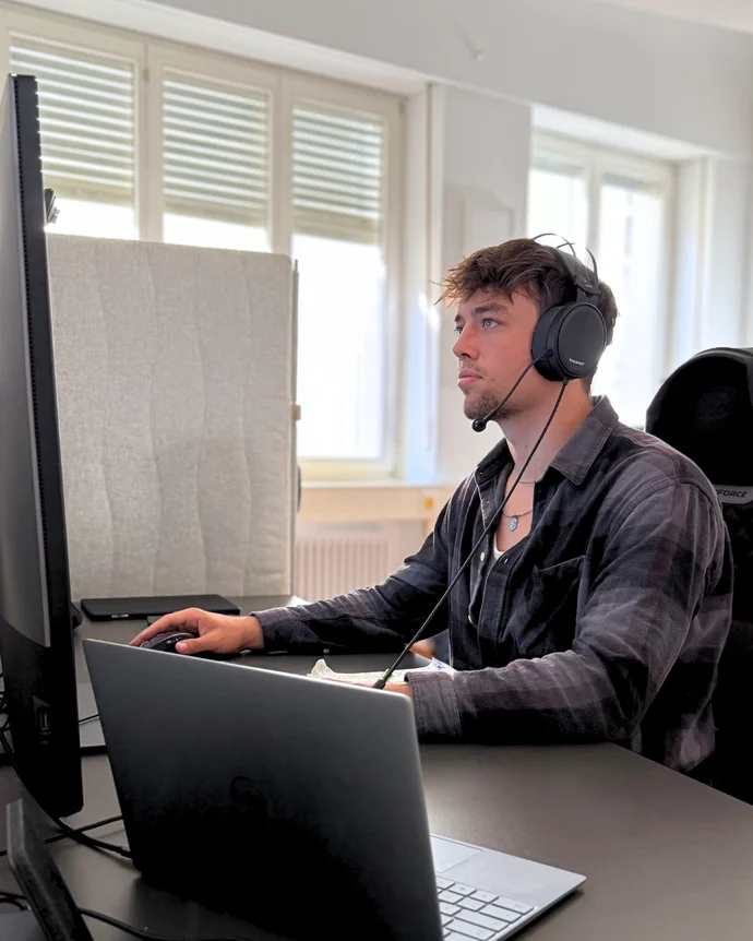 Mann mit Kopfhörern arbeitet konzentriert an Computerbildschirmen in einem Büro.