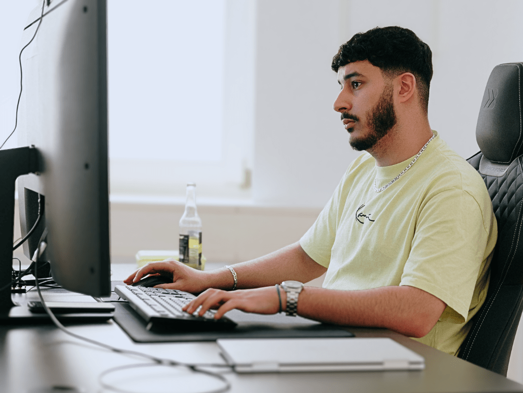 Mann am Computerarbeitsplatz mit Getränk in modernem Büro, vertieft in die Arbeit.
