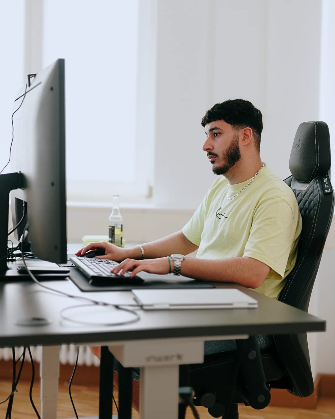 Mann am Computerarbeitsplatz mit Getränk in modernem Büro, vertieft in die Arbeit.