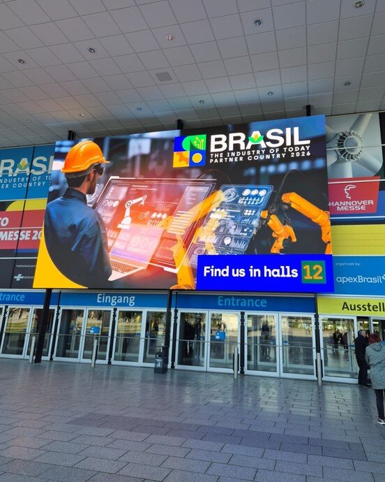 Digitale Werbetafel mit Brasilien-Motiv und Messehinweis, vor dem Eingangsbereich eines modernen Messegebäudes.