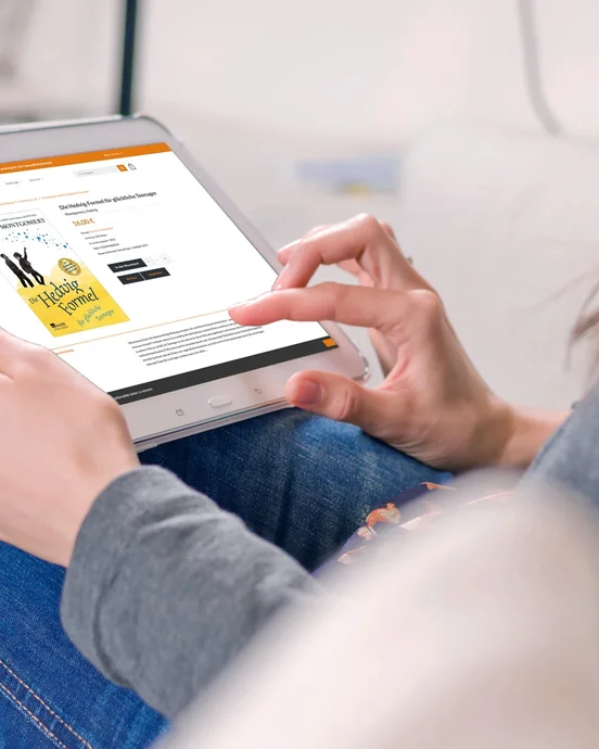 Person liest auf einem Tablet eine Buchrezension, während sie entspannt auf einem Sofa sitzt.