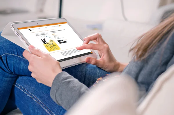 Person liest auf einem Tablet eine Buchrezension, während sie entspannt auf einem Sofa sitzt.