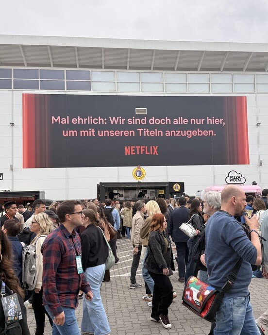 Menschenmenge vor einem Gebäude mit einem Netflix-Werbeschild, das humorvoll auf Titelwerbung hinweist.